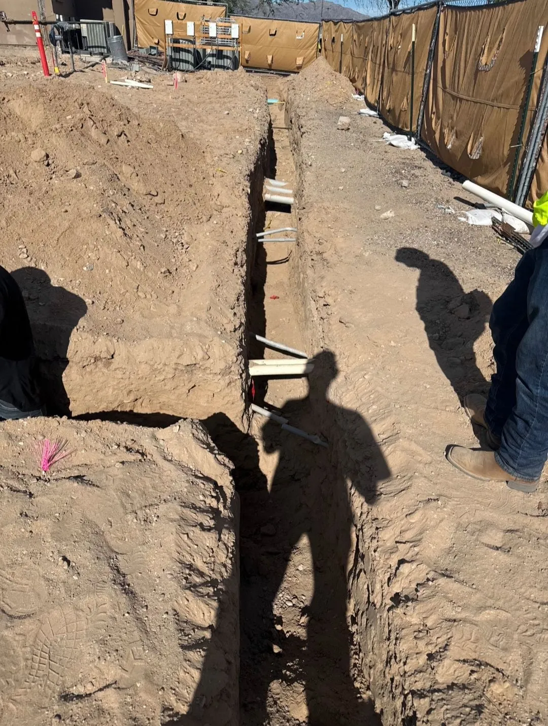 An open trench with new plumbing pipes laid across it at a construction site